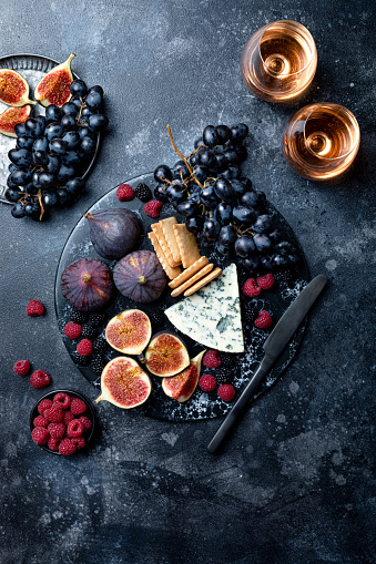 Appetizers, antipasti snacks and wine in glasses. Cheese and fruit platter on marble board over black background. Top view