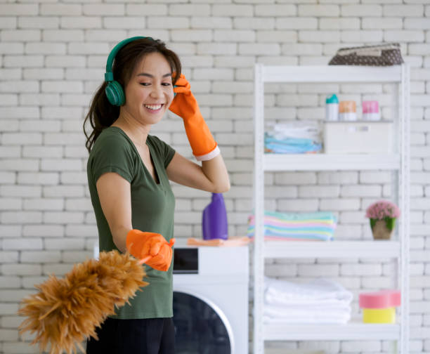 ama de casa asiática escuchando música de los auriculares verdes mientras limpia la sala de lavandería con "na plumero. - all laundry detergent audio fotografías e imágenes de stock