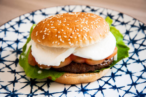 hamburger de style caprese garni de tranches de fromage mozzarella frais, tomate, feuilles de basilic et laitue sur brioche grillée sur plat en céramique traditionnel. sandwich maison et sain. style italien. - mozzarella caprese salad tomato italian cuisine photos et images de collection