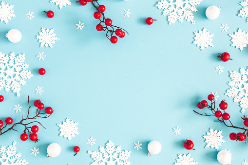 Front view of a red christmas ball hanging on a Christmas tree twig while snowing against a black background with copy space