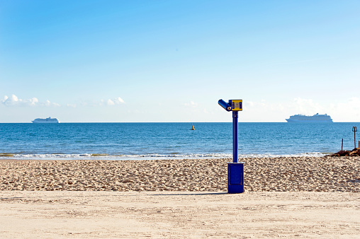 Ship shape promenade with amusement telescope looking out to sea with, empty beach huts and beaches, golden colours and muted blue and grey weather announce the onset of winter in Dorset during November