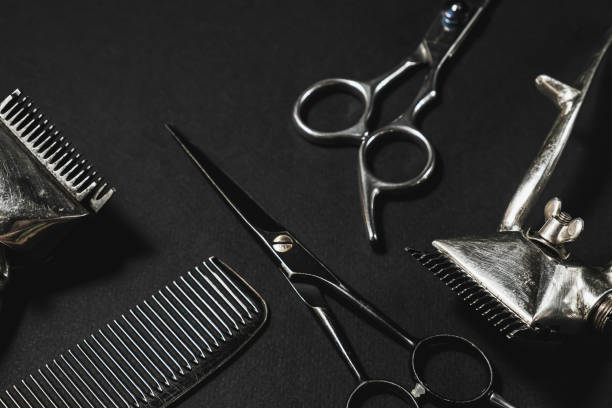 istock On a black surface are old barber tools. two vintage manual hair clipper, comb,hairdressing scissors. black monochrome. contrast shadows. Top view, flat lay. 1285650932