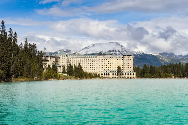 Lake Louise, Alberta, Canada - June 2018:  Wide angle view of the Fairmont Chateau Lake Louise hotel with snow capped mountains in the background and the emerald waters of Lake Louise in the foreground.