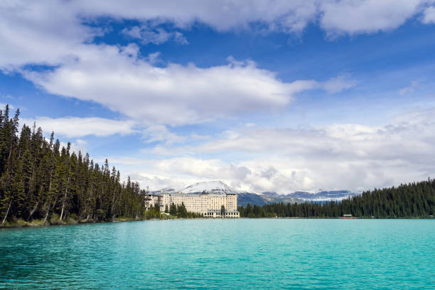 Lake Louise, Alberta, Canada - June 2018: : Wide angle view of the Fairmont Chateau Lake Louise hotel with snow capped mountains in the background and the emerald waters of Lake Louise in the foreground.