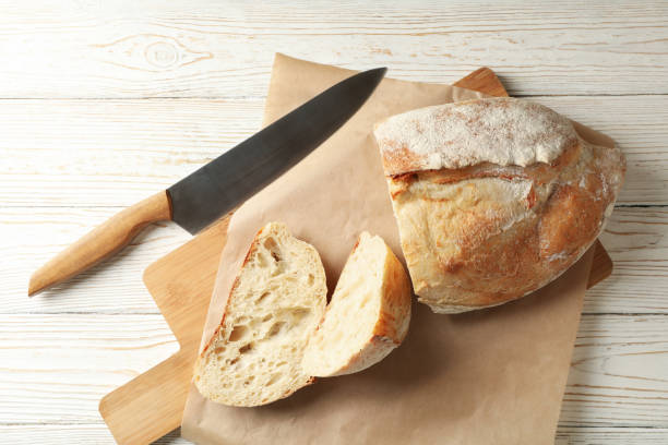 istock Baking paper with bread and knife on white wooden background 1285654927