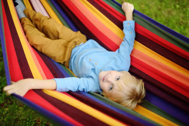 istock Cute little blond caucasian boy relaxing and having fun in multicolored hammock in backyard or outdoor playground. Summer active leisure for kids. Child swinging on hammock. 1285656487