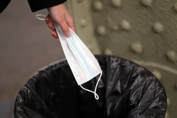 istock hand throwing a medical mask into a trash can 1285657219