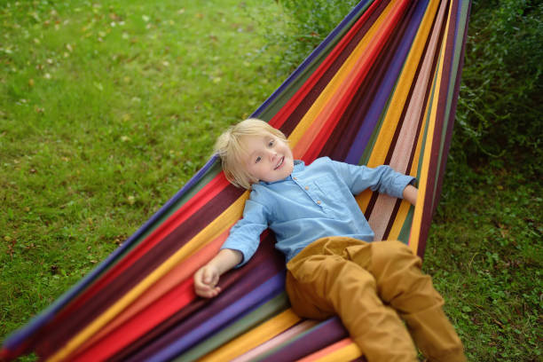 istock Cute little blond caucasian boy having fun with multicolored hammock in backyard or outdoor playground. Summer active leisure for kids. Child swinging and relaxing in hammock. 1285657302