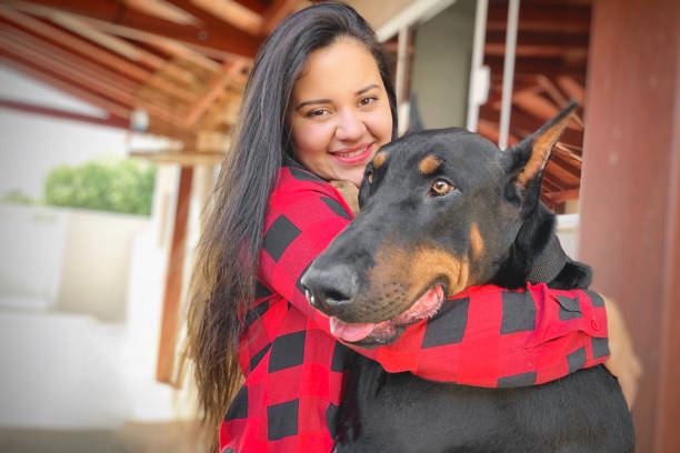 A Brazilian woman tenderly hugging her dog, a young Doberman, in her house. Behind them is her house, the garage and the gate on the background.