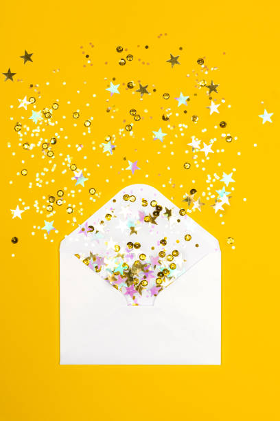 istock Sparkling confetti scattered from envelope on yellow background. 1285662997