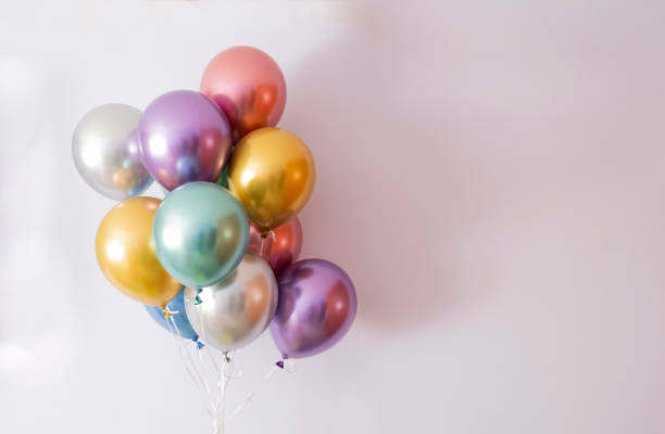 Photo of ten helium balloons in metallic colors on a mauve background, copy space on the right