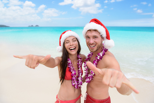 Christmas Hawaii vacation - Hawaiian beach couple wearing santa hat and doing welcome shaka sign happy at camera as welcoming gesture for winter holidays.
