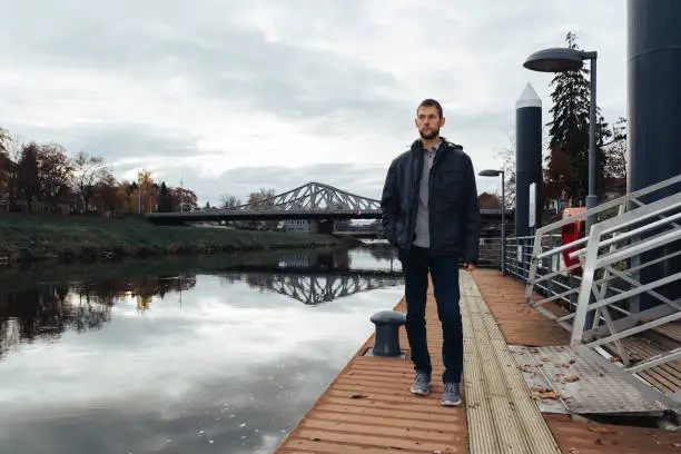 Portrait of young caucasian man in jacket walking on shipyard on Vltava river. Ceske Budejovice, Czech republic, toned photo