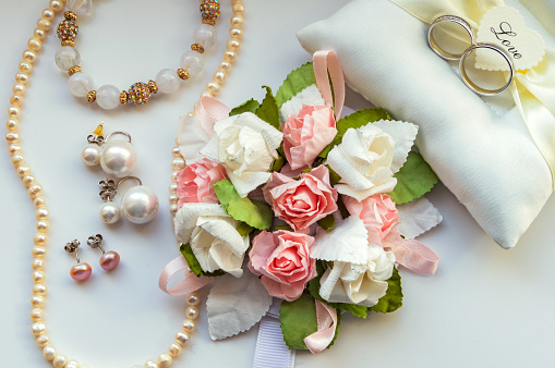 Beautiful set of wedding accessories for the bride. Bride's morning. Bride's bouquet of white and pink flowers. Pearl necklace and rings on the pillow
