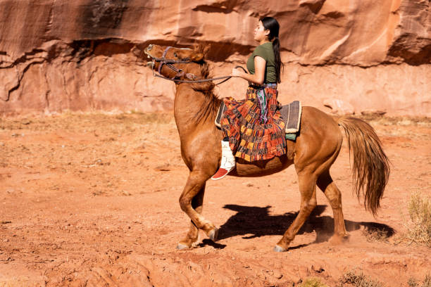 eine junge navajo frau in traditioneller kleidung reiten ihr pferd in der nähe von camel butte, monument valley, arizona - monument valley navajo mesa monument valley tribal park stock-fotos und bilder