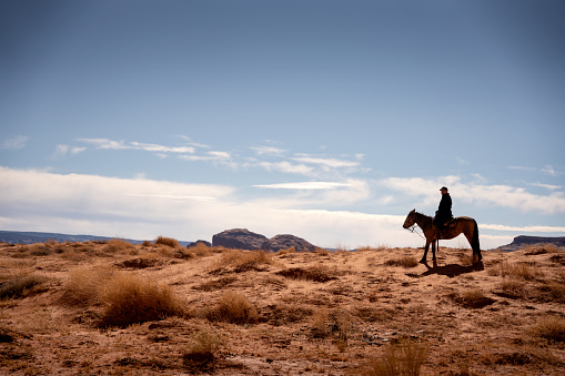 Hombre Hispano Maduro monta su caballo a través del escarpado desierto en el norte de Arizona cerca del Parque Tribal del Valle de Monuement en el país indio photo