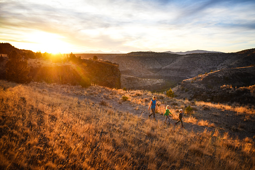 A mother and her two children hiking above a desert river canyon with a mountain range in the background. Crooked River, Oregon, USA.