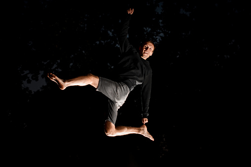 Man in black clothes having fun and jump high in the air at dark time