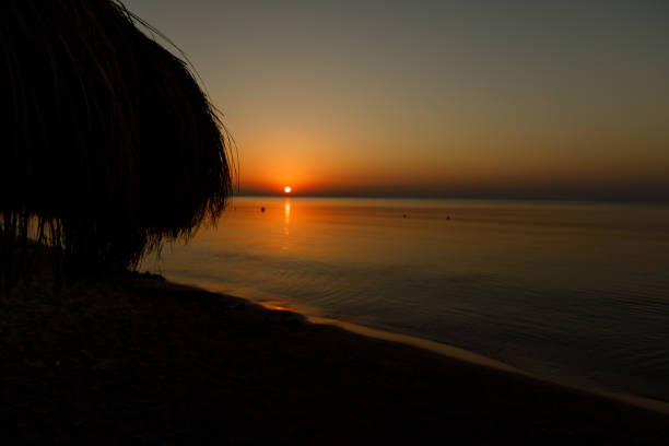 Copyspace of dramatic sunrise scene by a peaceful and calm beach. A parasol silhouette is visible on the left side.