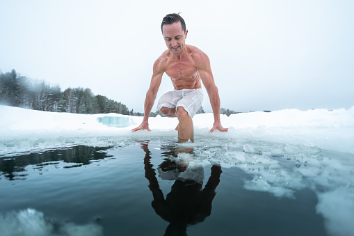 Young man swims in the ice hole made on the winter lake