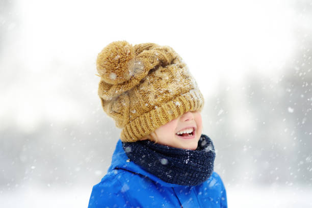 istock Funny little boy in blue winter clothes walks during a snowfall. Baby having fun while blizzard. Cute child wearing a warm hat low over his eyes. Outdoors winter activities for kids. 1285681698