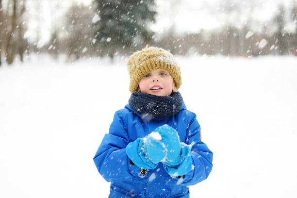 garotinho se divertindo brincando com neve fresca durante a queda de neve. luta de bola de neve. lazer ao ar livre ativo para crianças no dia de inverno nevado. - 11309 - fotografias e filmes do acervo