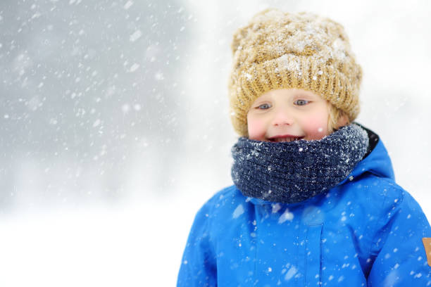 Portrait of a funny little boy in blue winter clothes walking during a snowfall. Baby having fun during a snowstorm. Cute child in a warm hat and scarf soiled in the snow. Outdoors winter activities Portrait of funny little boy in blue winter clothes walks during a snowfall. Baby having fun while blizzard. Cute child in a warm hat and scarf soiled in the snow. Outdoors winter activities for kids. 11313 stock pictures, royalty-free photos & images