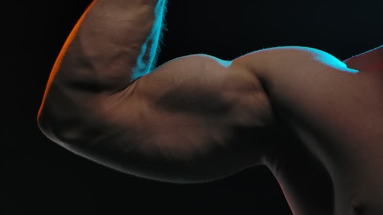 Professional athlete bodybuilder flexes the biceps on the arm, showing strong muscles. The concept of sports and body. Picture taken in the studio on a black background. Slow motion. Close up