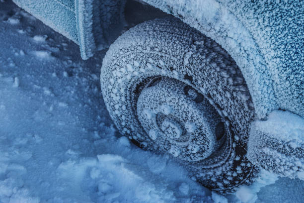 An SUV tire with an aggressive all terrain tread is stuck in fresh winter snow. There is some snow falling and visible against the dark areas of the vehicle.