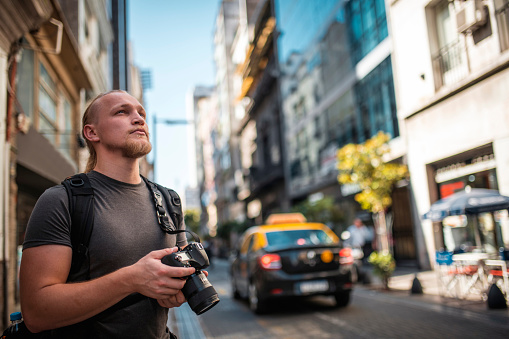 Caucasian blond tourist holding camera and photographing on city streets in Buenos Aires. He is holding camera and looking around.