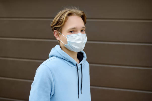 a teenage boy put on a face mask because the second wave of the covid-19 epidemic began. lockdown. the mask is the new standard for protection and prevention during a coronavirus or flu outbreak. - 11315 imagens e fotografias de stock