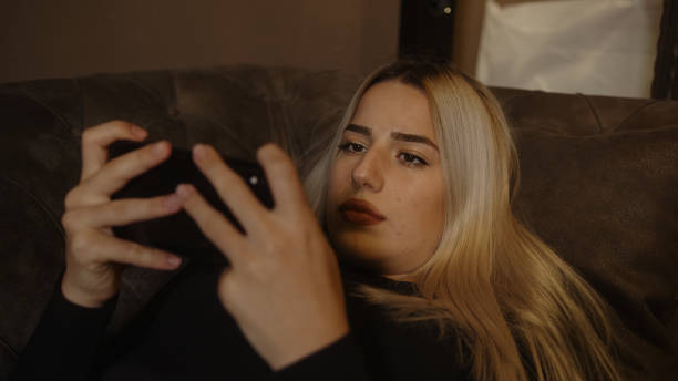 istock Young blond beautiful woman stretching on the sofa is playing game with smartphone and feeling sad 1285684784
