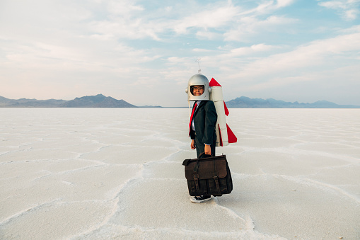 A young boy dressed in business suit, space helmet, and eyeglasses looks for new ideas, inventions and new business opportunities while wearing a rocket pack on the Utah salt flats. He looks to lead his business into the future with confidence.