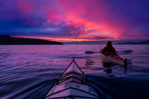 Adventure Man on a Sea Kayak is kayaking during a vibrant and colorful winter sunset. Taken in Vancouver, British Columbia, Canada. Adventure, Vacation Concept
