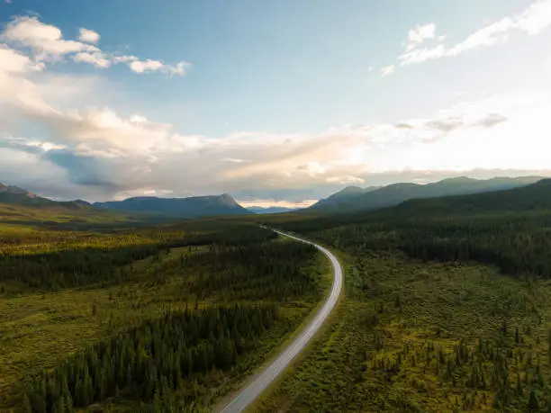 Beautiful View of Scenic Road surrounded by Forest and Mountains at Sunset. Aerial Drone Shot in Canadian Nature. Taken by Alaska Highway, Southern Yukon, Canada.