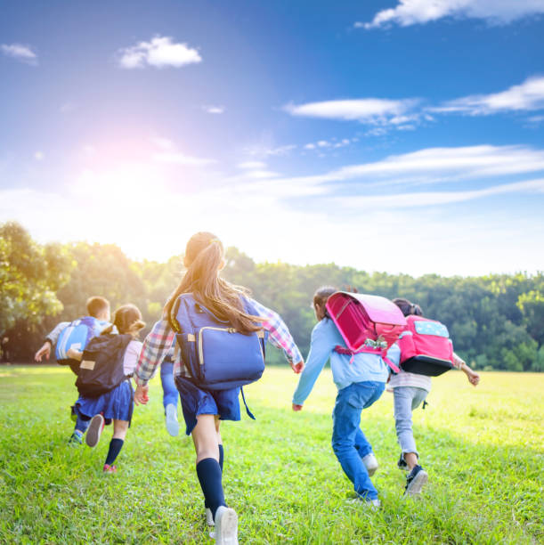 rear view of elementary school kids running on the grass - elementary age child group of people togetherness imagens e fotografias de stock