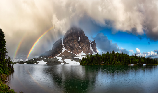 Beautiful panoramic View of the Iconic Canadian Rocky Mountain Landscape. Dramatic Sky with Rainbow. Taken near Banff, boarder of British Columbia and Alberta, Canada. Nature Background Panorama