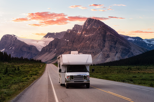 Scenic road in the Canadian Rockies during a vibrant sunny summer sunrise. White RV Driving on route. Taken in Icefields Parkway, Banff National Park, Alberta, Canada.