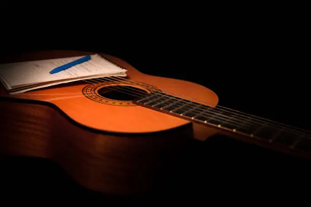 Created in the studio under a warm light this songwriting idea shows an acoustic guitar body and a writing pad along with a pen for composers and lyricists.