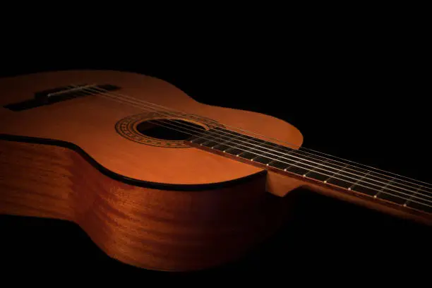 This studio shot of an acoustic guitar body is warmly lit on a clean black background. Plenty of room for copy, ideal for guitar lessons, training and music courses concepts.