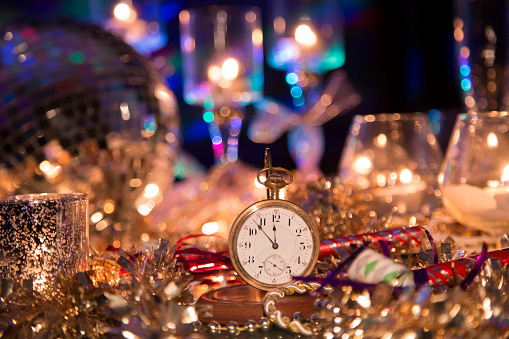 New Year's Even holiday party with lights and candles.  Centerpiece of image is an antique pocket watch with time set at almost midnight.