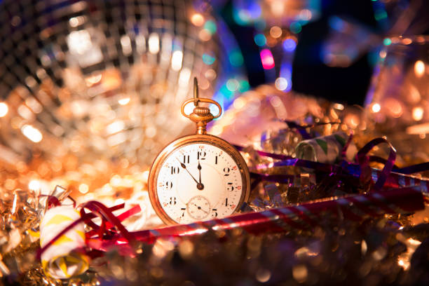 New Year's Eve holiday party, pocket watch, clock at midnight. New Year's Even holiday party with lights and candles.  Centerpiece of image is an antique pocket watch with time set at almost midnight. party blower stock pictures, royalty-free photos & images