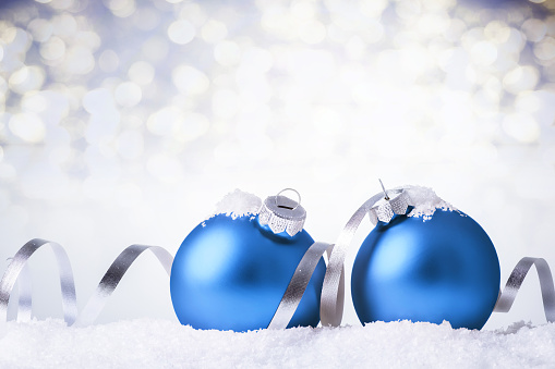 Blue christmas balls with silver ribbon in snow over bokeh lights background, with copy space.