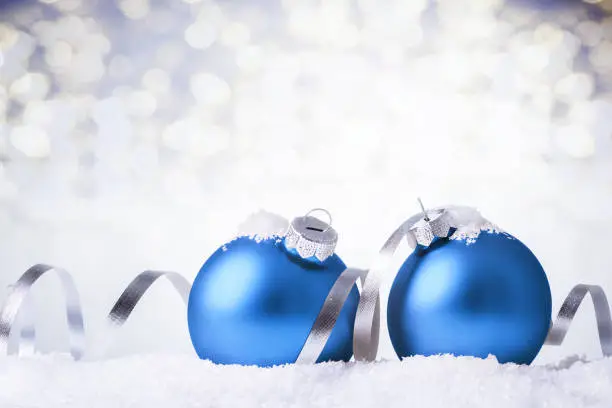 Blue christmas balls with silver ribbon in snow over bokeh lights background, with copy space.