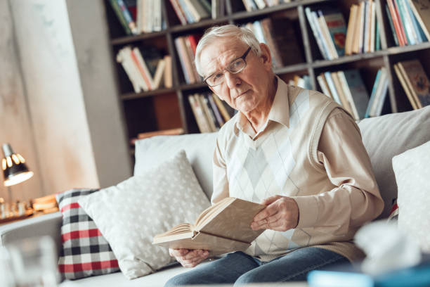 istock Senior man alone sitting at library in eyeglasses holding book thoughtful 1285702987
