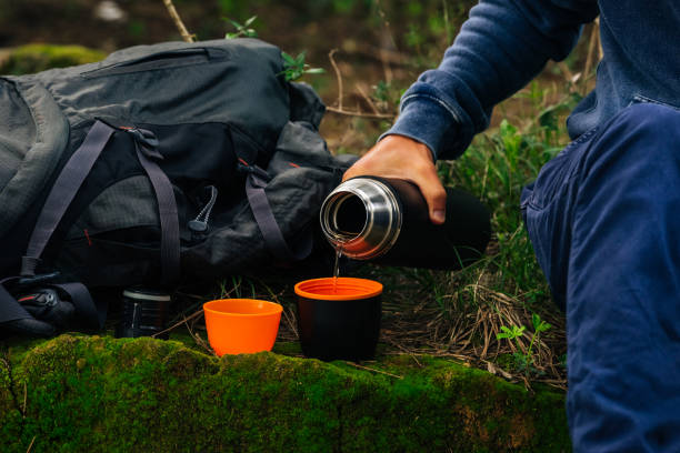 istock Drinking tea during hike. Man hand pouring hot tea from black thermos bottle into 2 cup's in the woods. Refreshment during hiking. Camping equipment 1285704378