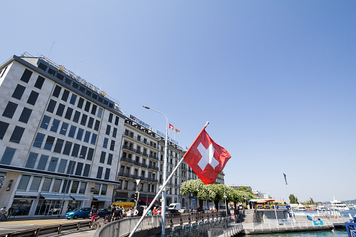 Picture of the Swiss flag in front of the Leam lake in Geneva, Switerland, in front of the Quai du Mont Blanc street. It is the main waterfront of the city of Geneve.