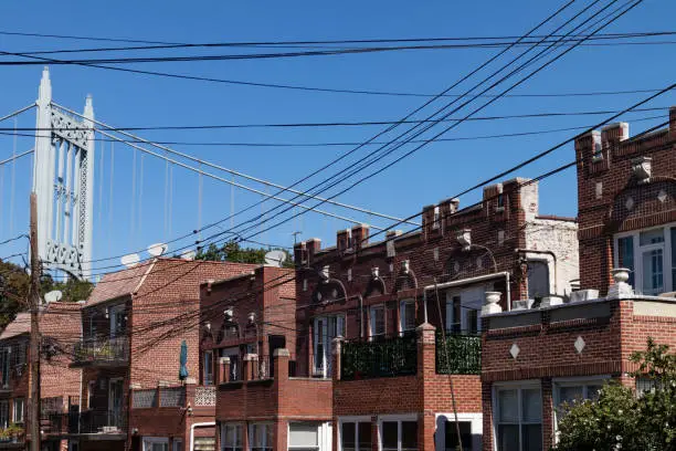 A row of similar brick homes and telephone wires with the Triborough Bridge in the background in Astoria Queens of New York City