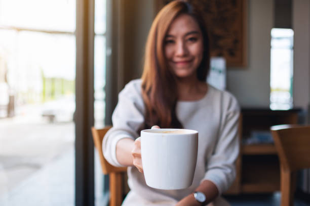 a beautiful young asian woman holding and giving a cup of hot coffee in cafe Closeup image of a beautiful young asian woman holding and giving a cup of hot coffee in cafe beautiful women giving head stock pictures, royalty-free photos & images