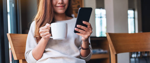 istock a beautiful asian woman holding and using mobile phone while drinking coffee in cafe 1285724351
